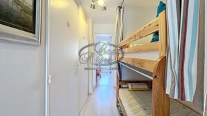 A narrow hallway with a bunk bed on the right, a door at the end, and a ceiling light fixture.