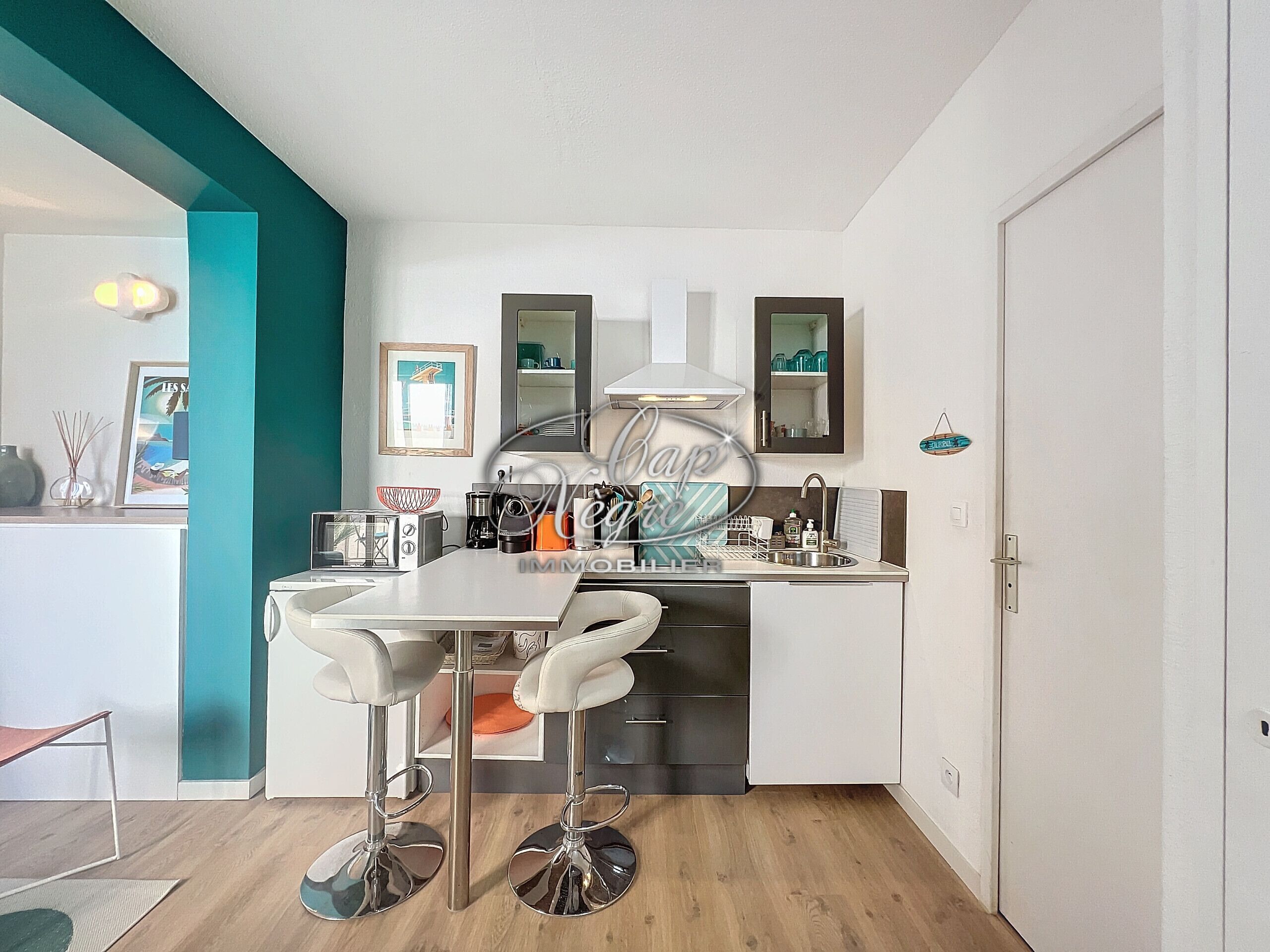 A modern kitchen with white cabinets, a stainless steel sink, and two bar stools.