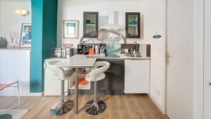 A modern kitchen with white cabinets, a stainless steel sink, and two bar stools. - Modern studio with sea view and direct access to Cavalière Beach (Le Lavandou)