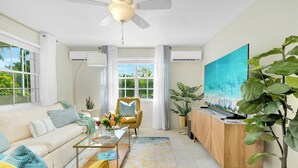 Un salon moderne avec un canapé, des fauteuils, une table basse, un téléviseur et de grandes fenêtres.