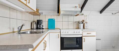 A compact kitchen with white cabinets, a stove, and a coffee maker.
