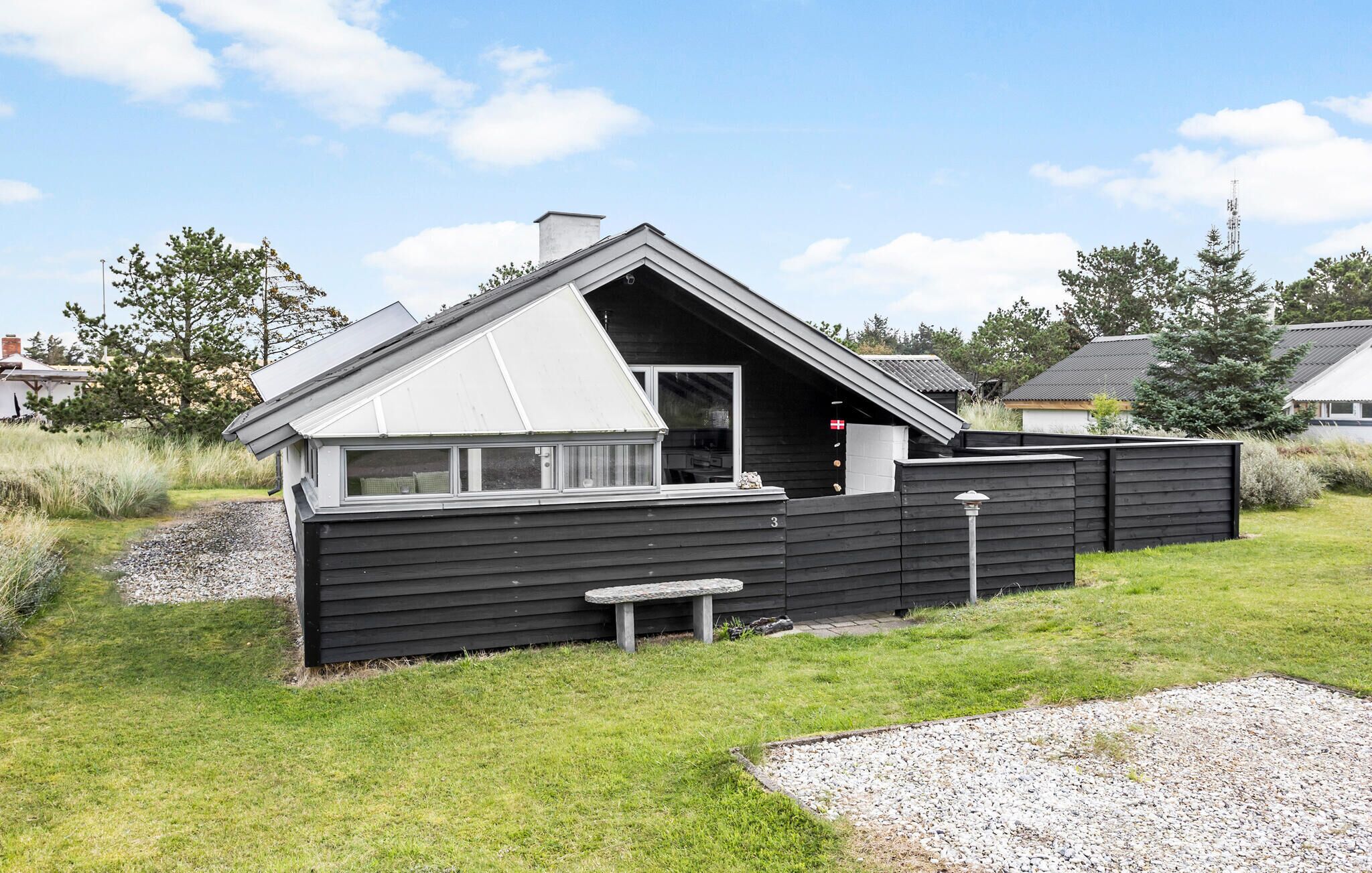 A modern, single-story cabin with a sloped roof, a small porch, and a stone bench.