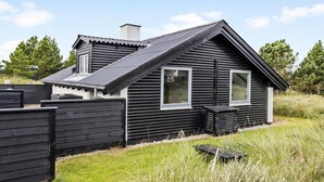Een donker houten chalet met schuin dak, twee ramen en een schoorsteen.