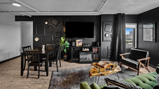 Ein modernes Wohnzimmer mit Essbereich, einem großen Flachbildfernseher und Blick auf die Stadt durch ein Fenster.