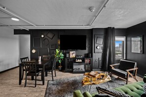 A modern living room with a dining area, a large flat-screen TV, and a view of the city through a window. - Stunning Penthouse - King Bed - City/River View - Corner Unit - Wells Fargo (Des Moines)