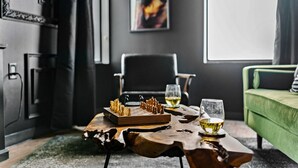 Ein modernes Wohnzimmer mit Schachbrett, zwei Weingläsern, einem grünen Sofa und einem Bild an der Wand.