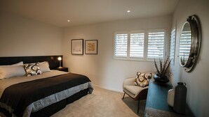 A bedroom with a bed, nightstands, a chair, a mirror, and a window with blinds. - The Heights  (Wanaka)