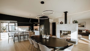 A modern kitchen with a central island, a dining area with a dark wooden table and grey chairs, and a fireplace with a white mantel. - The Heights  (Wanaka)