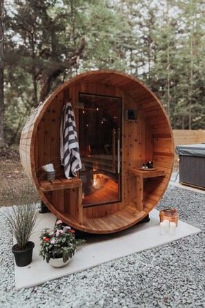 A wooden hot tub with a glass door, surrounded by potted plants and a small table with candles.