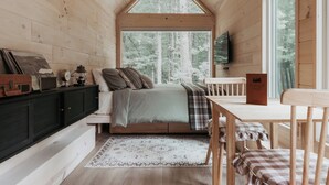Un intérieur de chalet chaleureux avec un lit en mezzanine, une table à manger et un téléviseur fixé au mur.