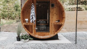 Un sauna en bois avec une porte, un porte-serviettes et une petite étagère où sont posées des bouteilles.