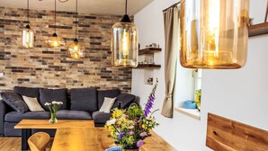 A modern living room with a wooden dining table, a sofa, and hanging pendant lights. - Slunečná by Interhome (Horni Plana)