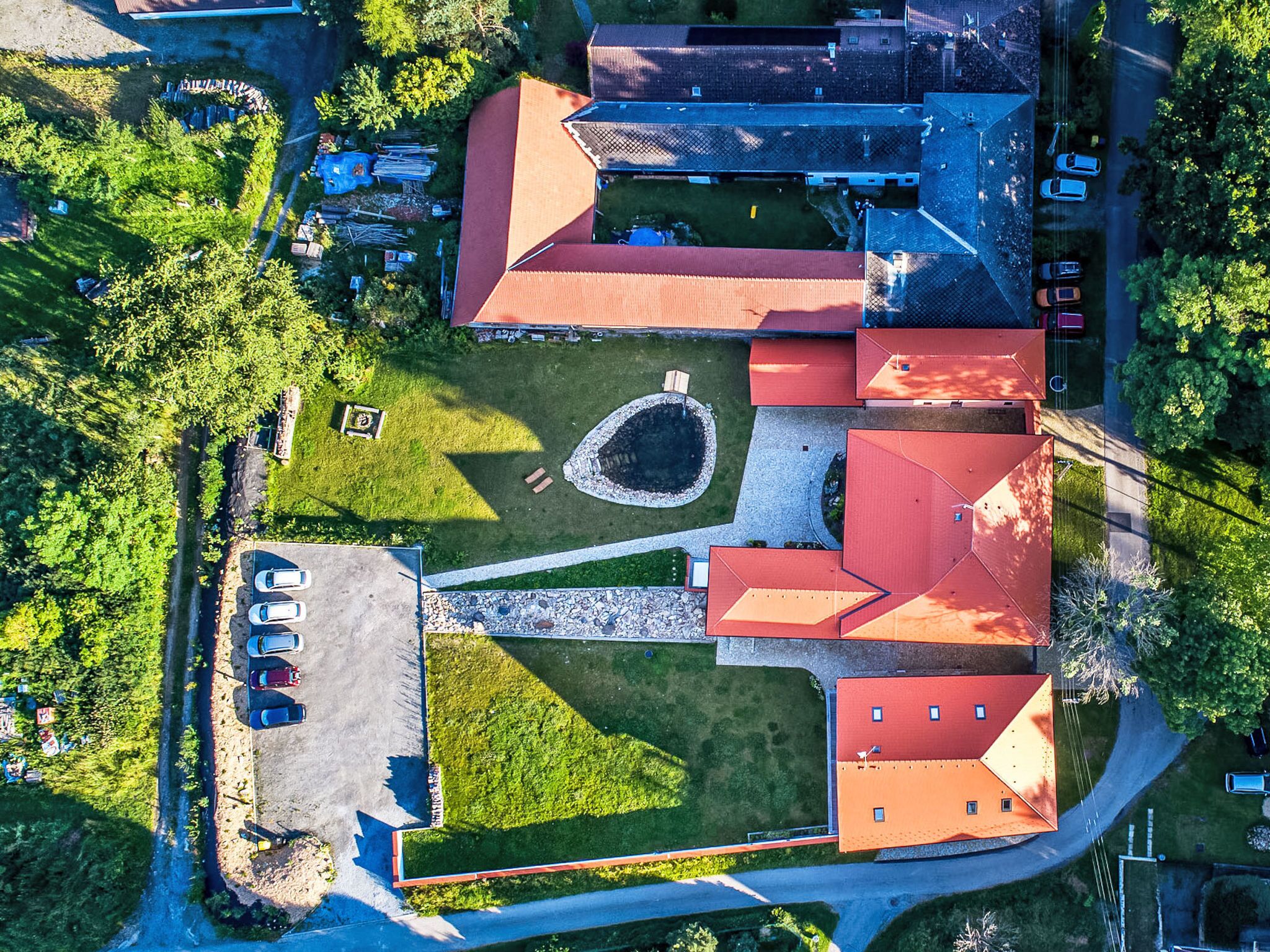 Vista aérea de un edificio con varias secciones de tejados rojos, un patio central y vegetación circundante.