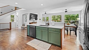 Une cuisine spacieuse avec des meubles de couleur verte, un lave-vaisselle et un coin repas comprenant une table et des chaises.