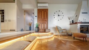 Een moderne woonkamer met een houten vloer, een ingebouwde zithoek met verlichting en een houten deur, plus een wandklok.