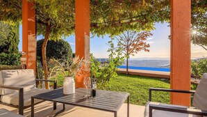 Een terras met een tafel en stoelen, een vaas met gedroogde planten en uitzicht op een waterpartij en het landschap in de verte.