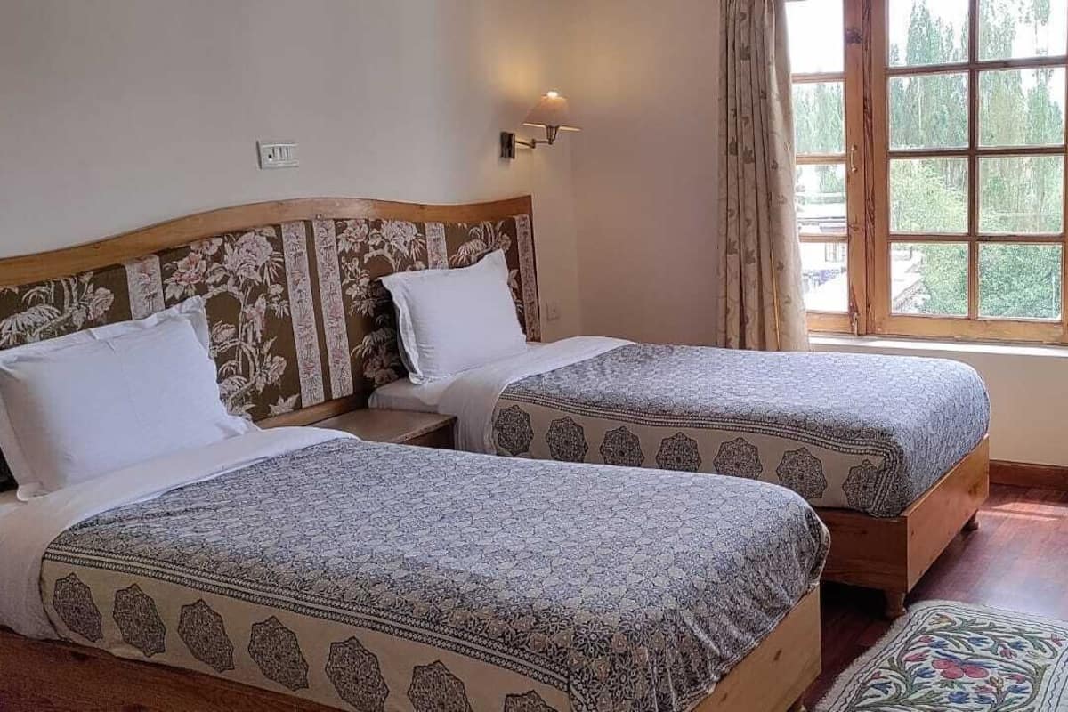 Een kamer met twee bedden, een houten hoofdeinde, een raam met gordijnen, een kleine tafel en een stoel.