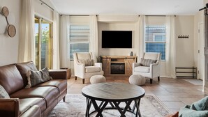 Ein geräumiges Wohnzimmer mit einer Ledersofa, zwei Sessel, einem runden Couchtisch, einem Kamin und einem Deckenventilator.