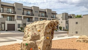 A climbing wall with holds in a sandy area, with modern buildings in the background. - Newly furnished 5bd/4.5ba Townhome - The Vue 30 welcomes you! (St. George)