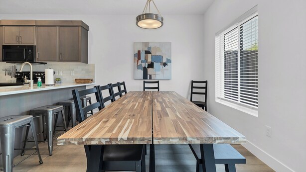 A modern kitchen with built-in appliances, a wooden dining table with chairs, and a large window with blinds. - Newly furnished 5bd/4.5ba Townhome - The Vue 30 welcomes you! (St. George)