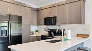 A modern kitchen with stainless steel appliances, a large island with a sink, and light wood cabinetry. - Newly furnished 5bd/4.5ba Townhome - The Vue 30 welcomes you! (St. George)