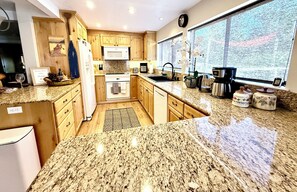 A kitchen with granite countertops, wooden cabinets, a microwave, a sink, and a window with a view.