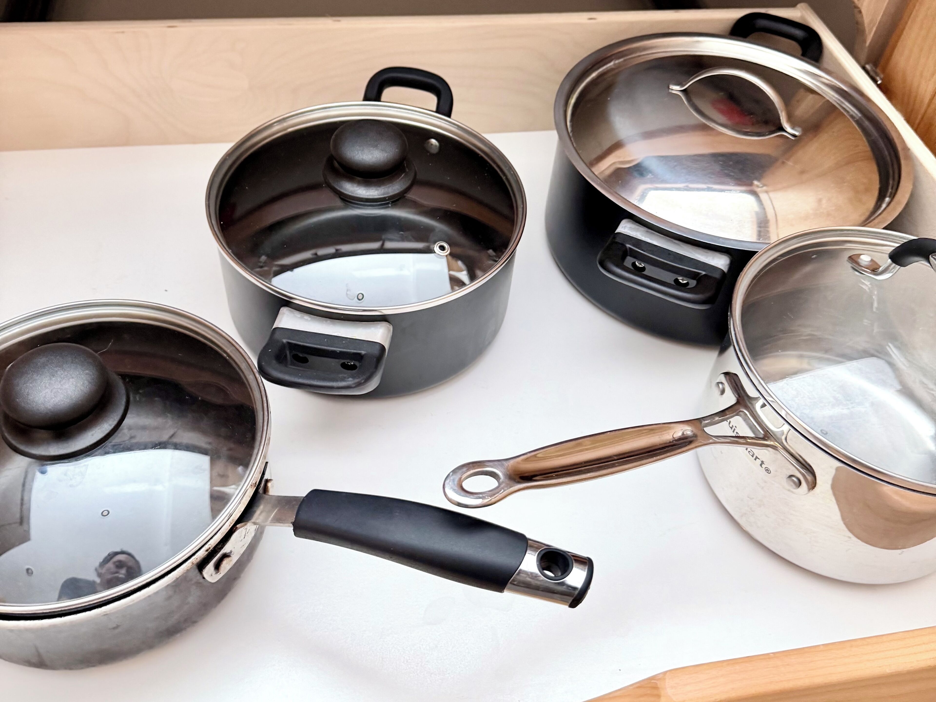 Four stainless steel pots with lids and handles on a white countertop.