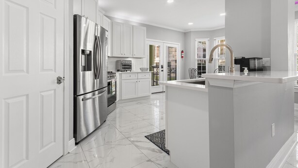A modern kitchen with white cabinetry, stainless steel appliances, and a marble floor.