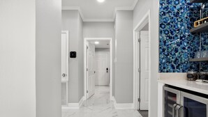 A hallway with a marble floor, white walls, and a blue hexagonal tile backsplash.