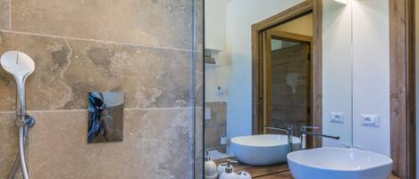 A modern bathroom with two large white sinks, a glass shower enclosure, and a wooden vanity.
