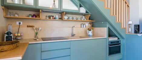 A modern kitchen with teal cabinetry, a wooden staircase, and a built-in oven.