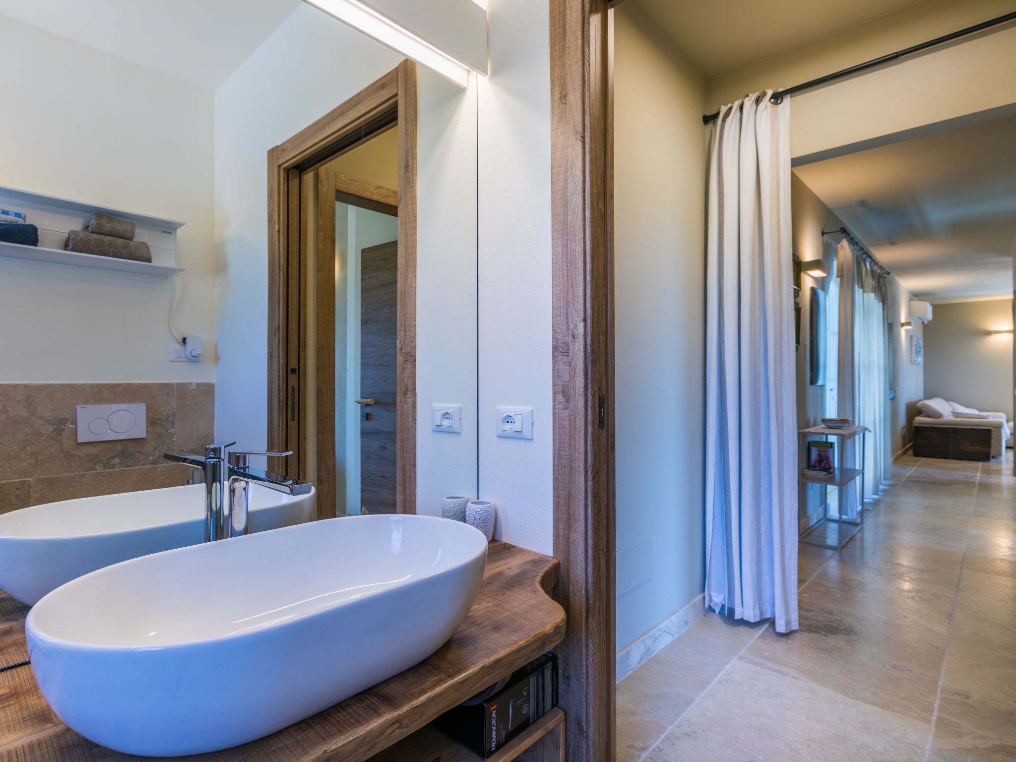 A modern bathroom with two large sinks, a wooden vanity, and a shower area with a curtain.