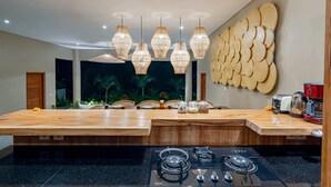 A modern kitchen with a central island, overhead pendant lights, and a decorative wall piece. - Villa Canopy (Tabanan)