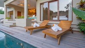 A poolside area with wooden lounge chairs and a view of the pool. - Villa Canopy (Tabanan)