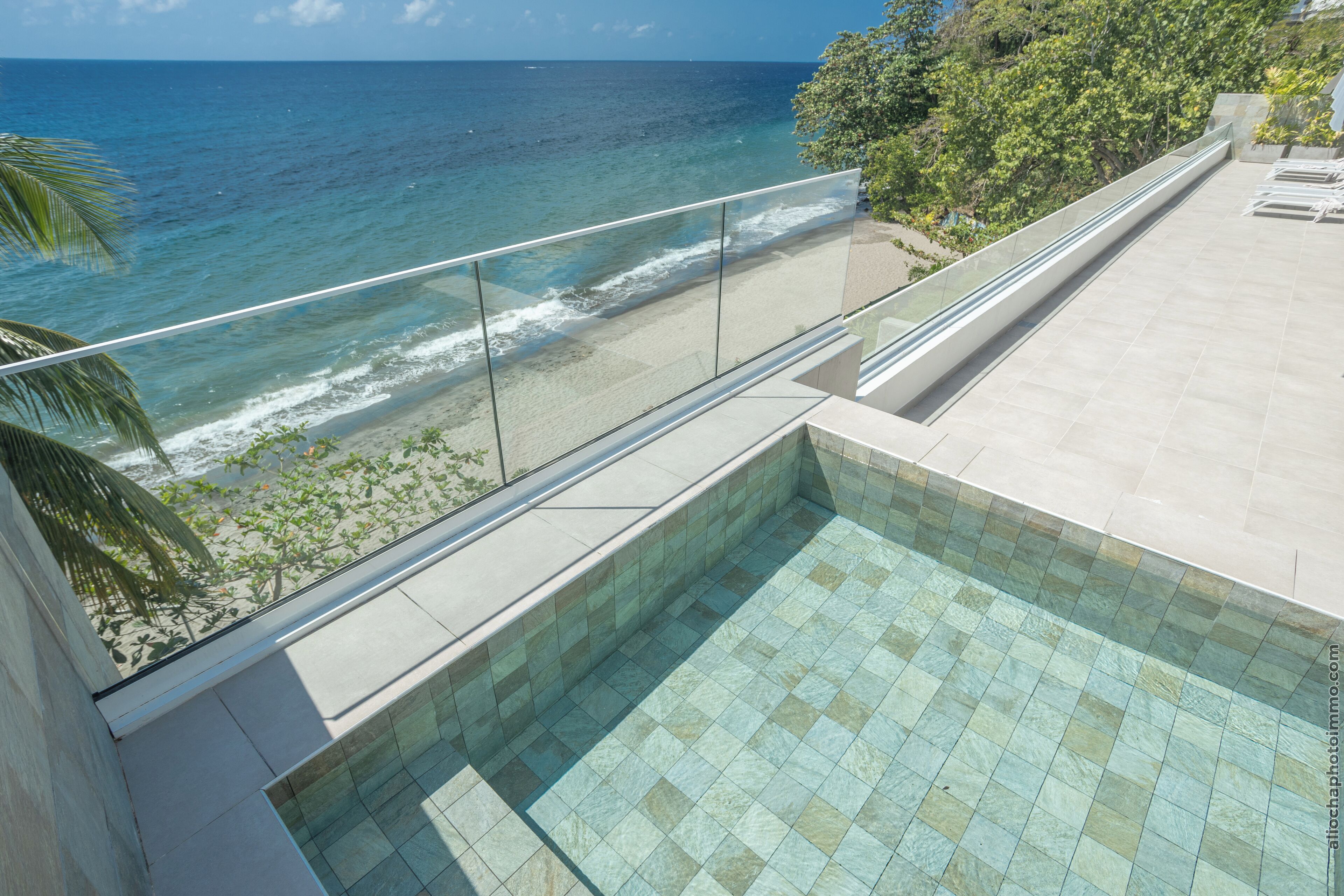 A rooftop pool with a glass balustrade overlooking a beach and ocean.