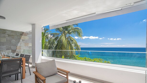 Un balcon avec vue sur l’océan et les palmiers, aménagé avec une table, des chaises et un canapé.