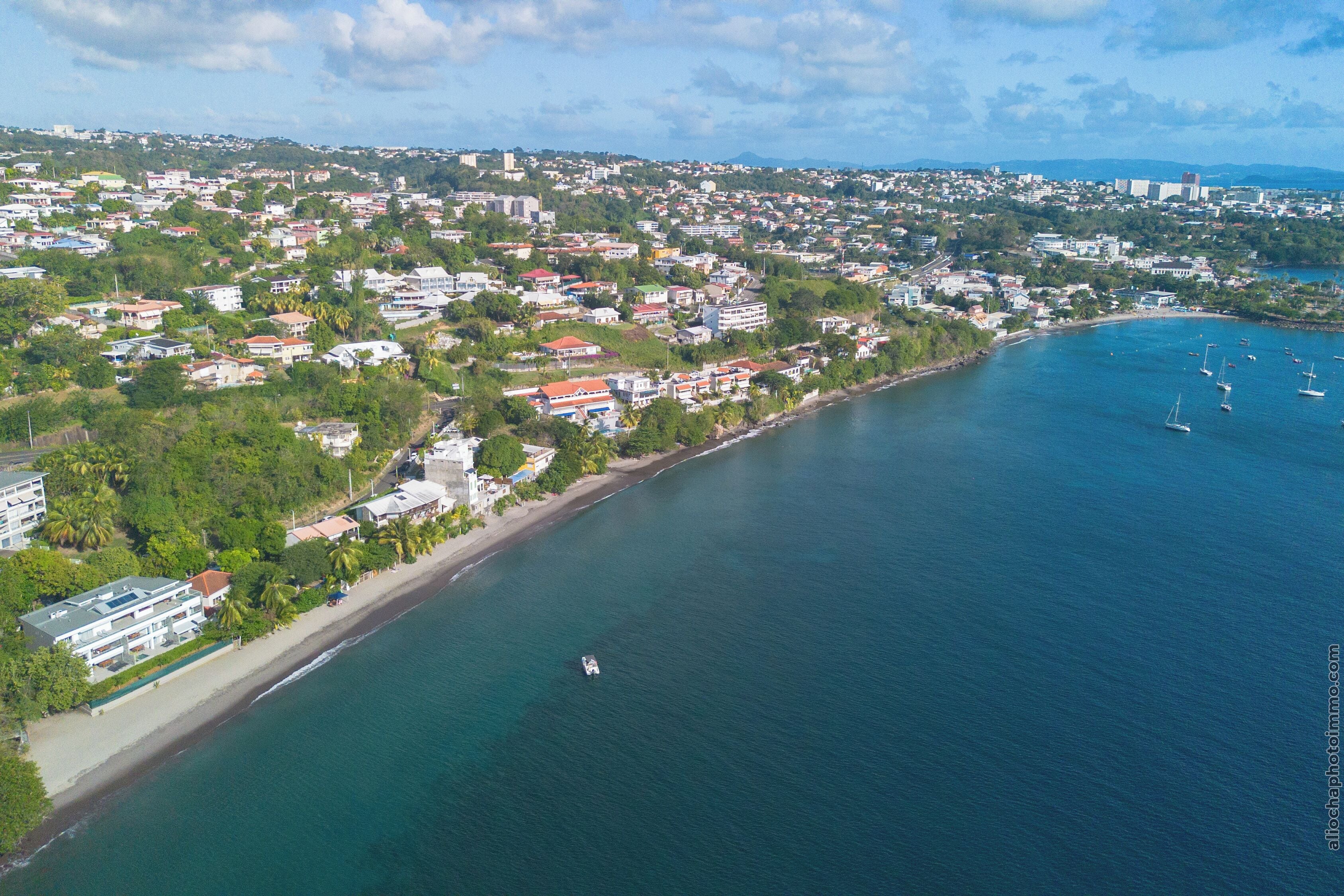 Una vista aerea di una città costiera con spiaggia, edifici residenziali e barche nell'acqua.