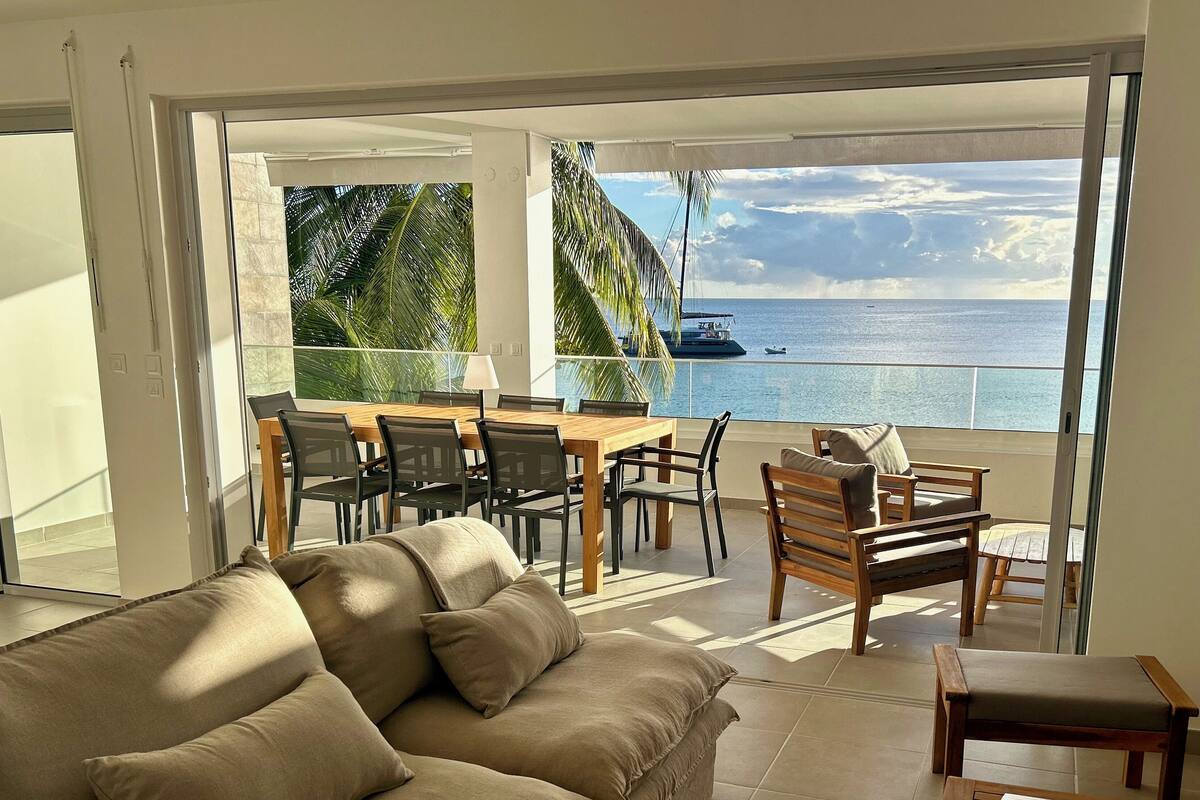 Ein modernes Wohnzimmer mit Sofa, Esstisch, Stühlen und Blick aufs Meer.