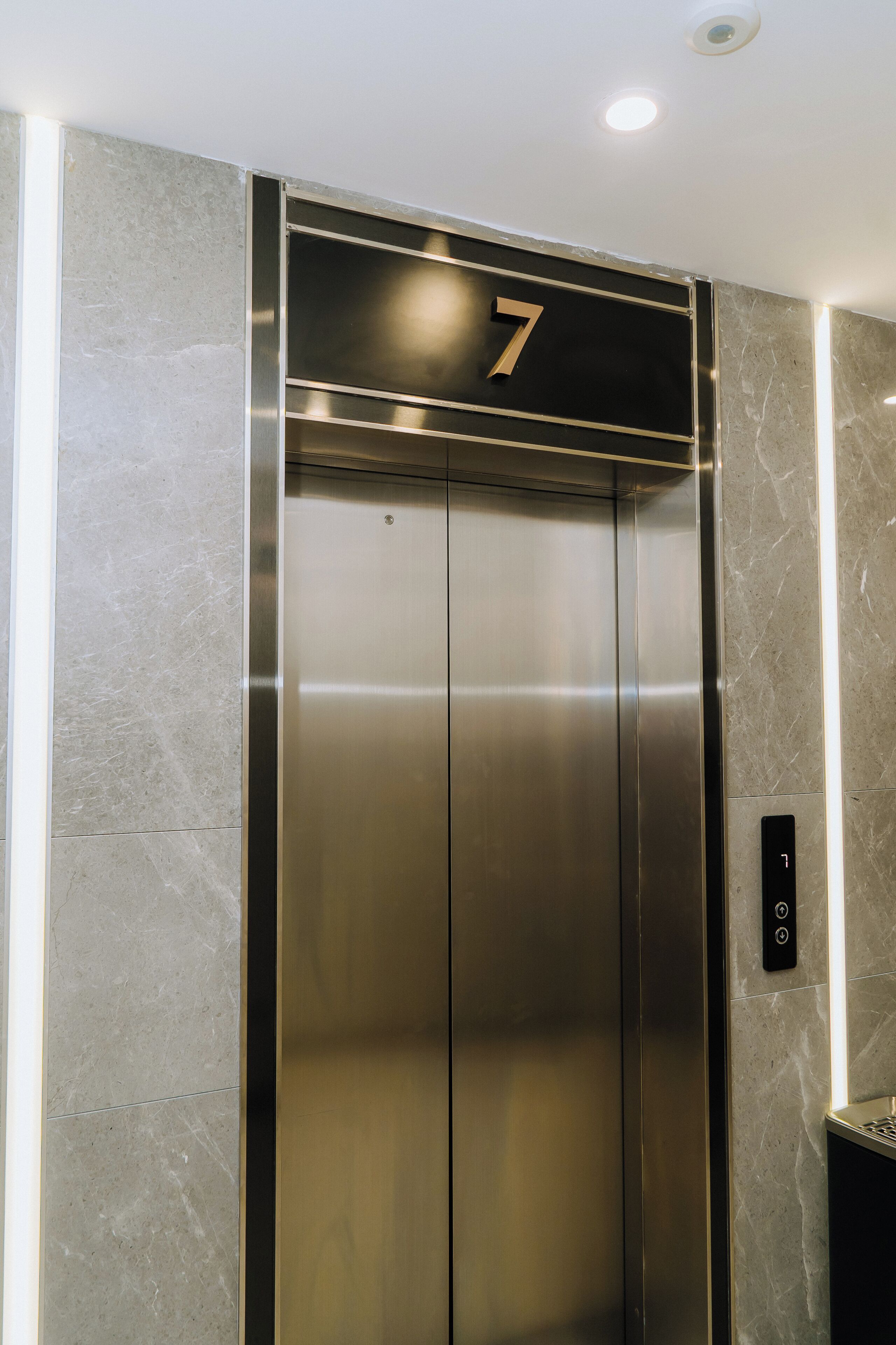 Een moderne lift met een metalen afwerking en een bordje met het cijfer 7 erboven.