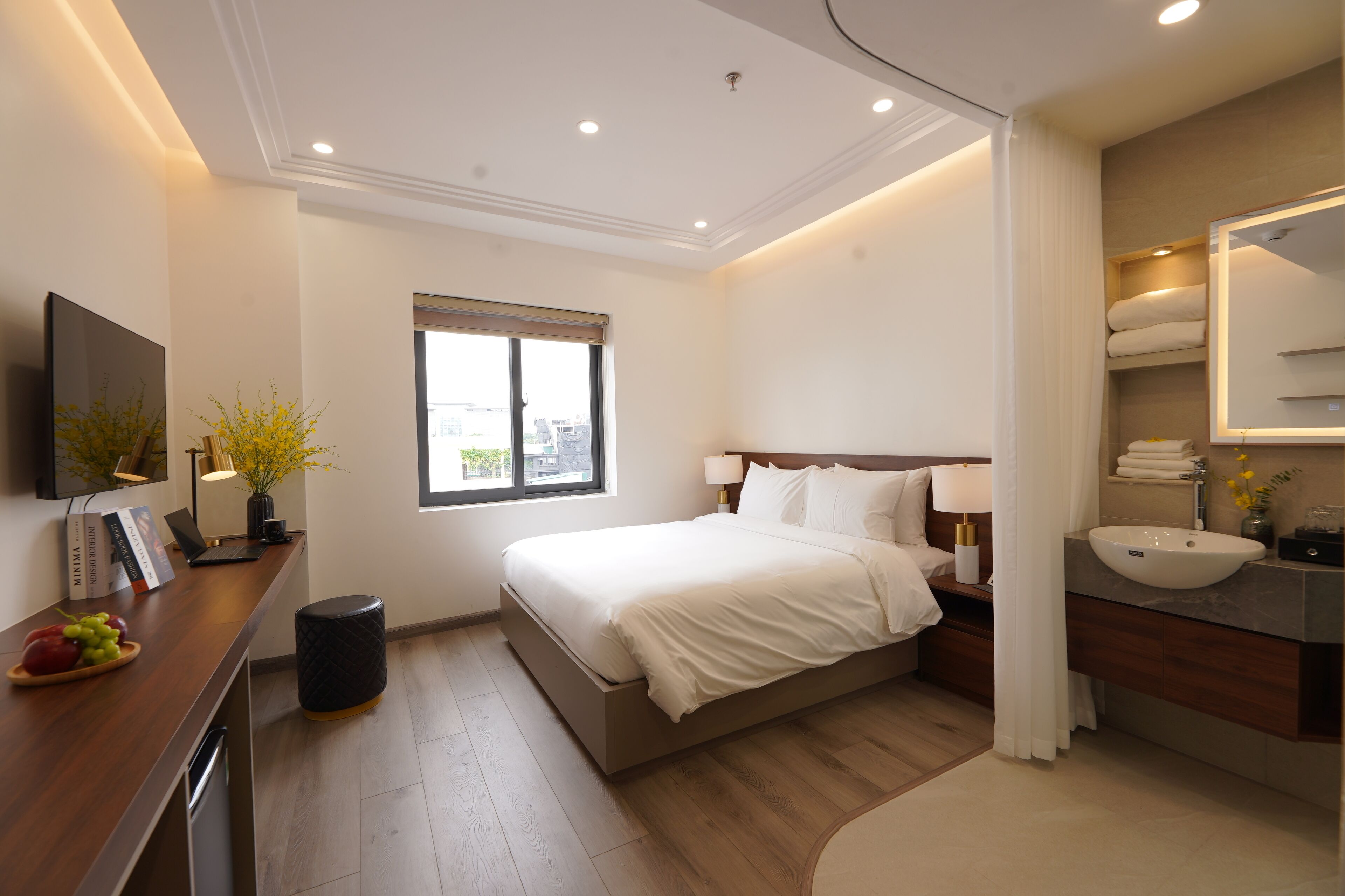A modern hotel room with a large bed, bedside table, lamp, and a bathroom with a sink and mirror.