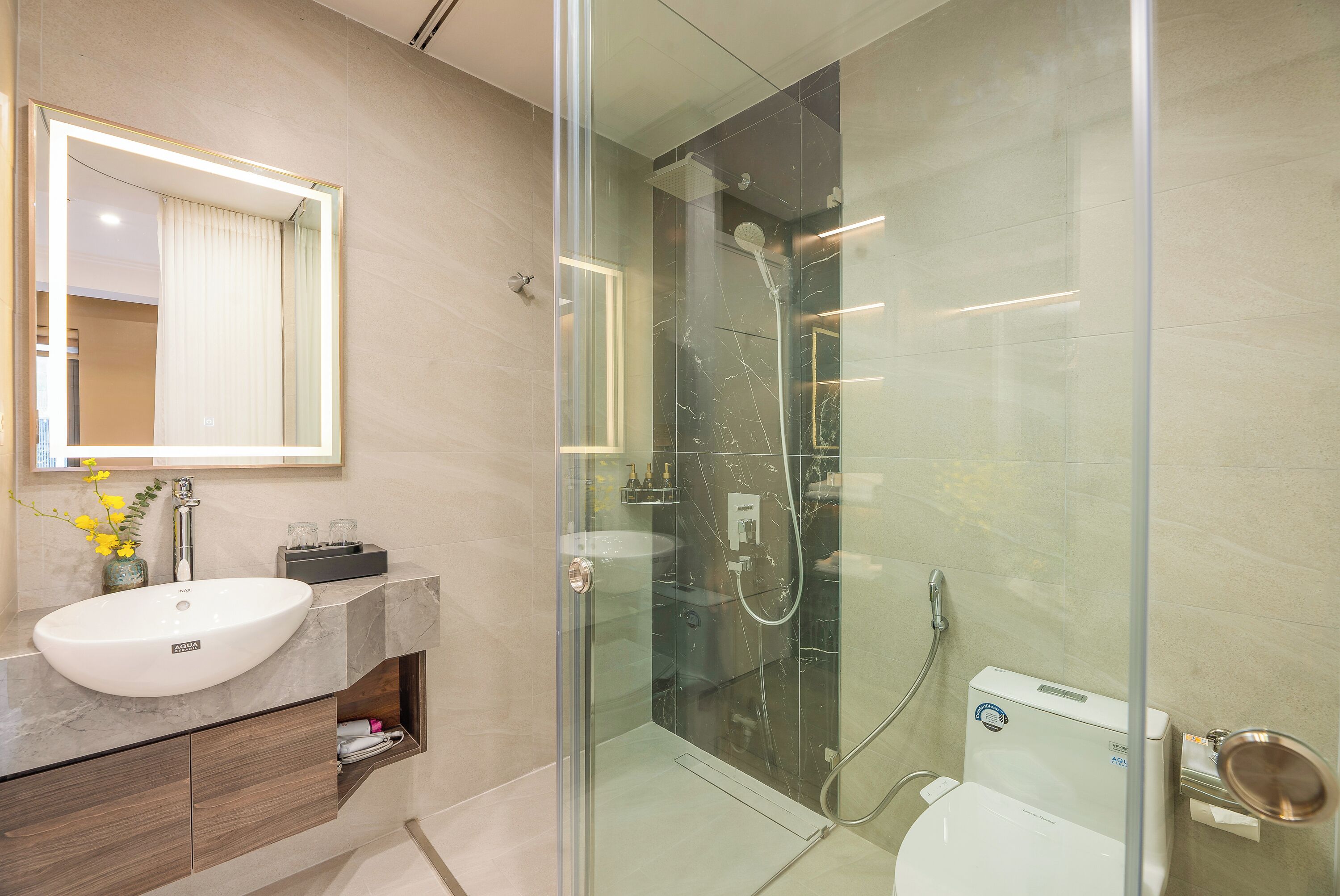 Une salle de bain moderne avec une douche à parois de verre, un lavabo blanc et un plan de toilette en marbre.