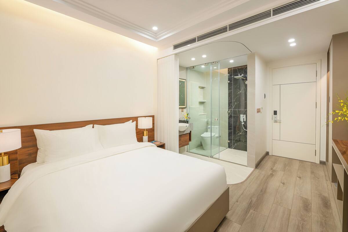 A hotel room with a large bed, bedside lamps, a glass-enclosed shower, and a wooden floor.
