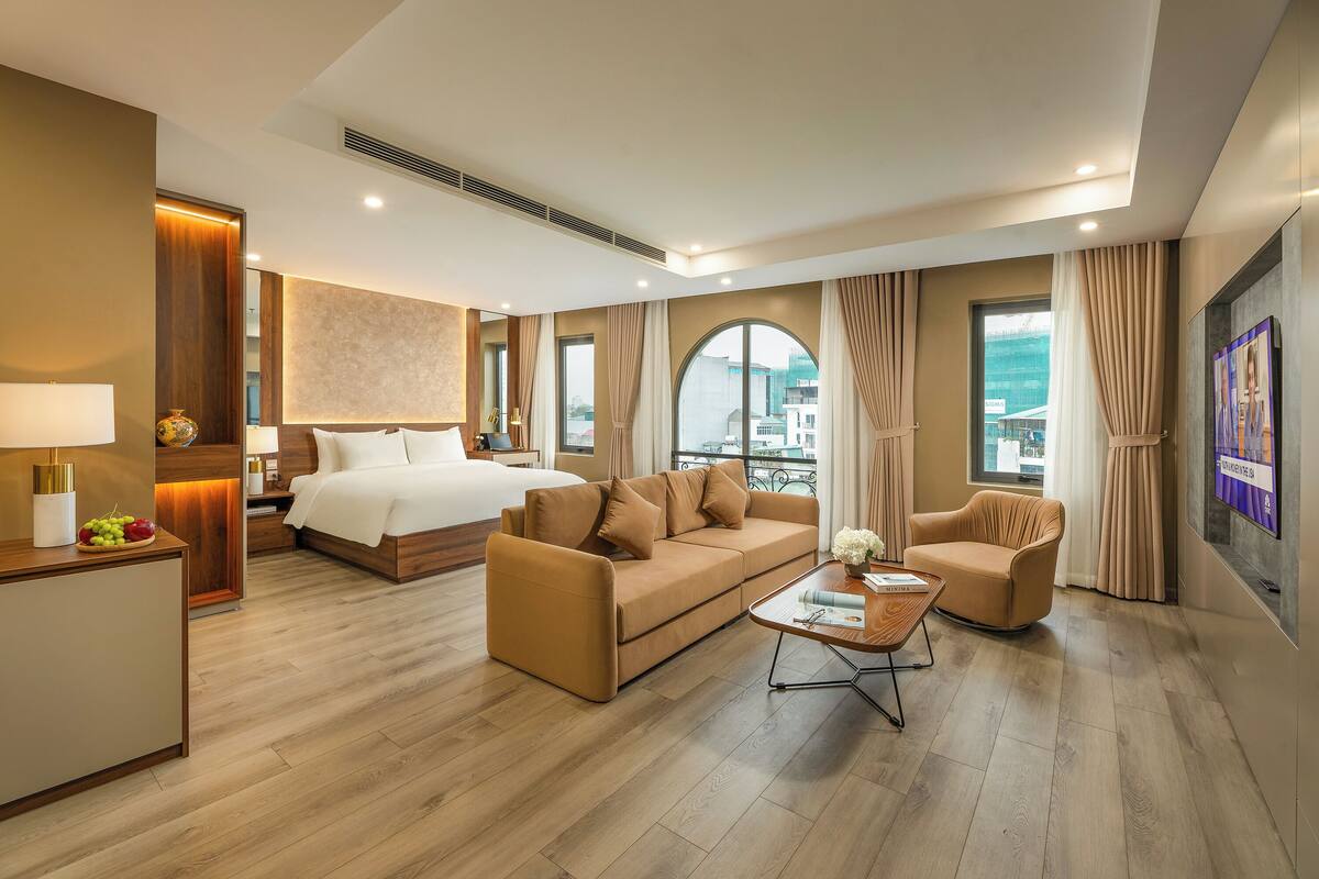 A modern hotel room with a bed, sofa, armchair, and a small table.