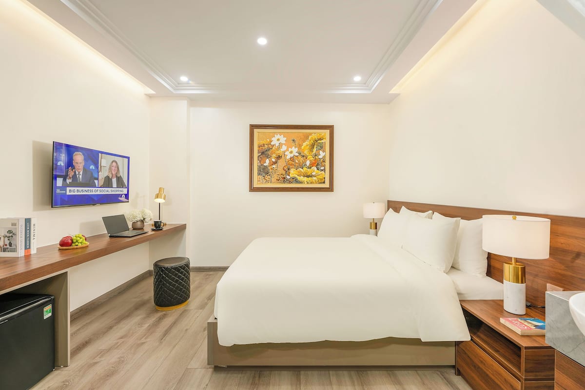 A hotel room with a bed, bedside table, lamp, and a TV displaying a news program.