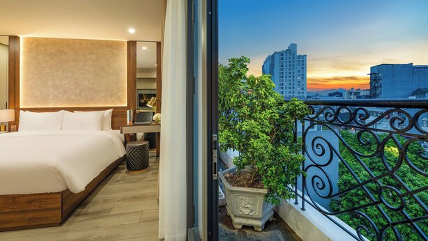 A hotel room with a large bed, bedside table, lamp, and a potted plant. -  Gilson Hanoi Hotel (Hanoi)