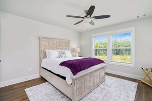 A bedroom with a bed, a ceiling fan, a window, and a view of greenery outside.