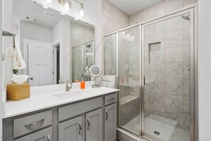 A modern bathroom with a glass-enclosed shower, a large mirror, and a white sink.