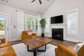 Een woonkamer met een open haard, een televisie en een groot raam met zonwering.