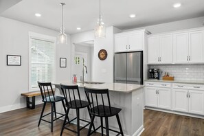 A modern kitchen with white cabinets, a stainless steel refrigerator, and a bar area with black stools.