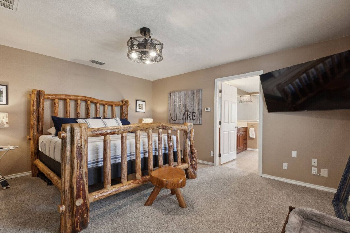 A bedroom with a rustic wooden bed frame, a small wooden stool, a ceiling light fixture, and a television mounted on the wall.